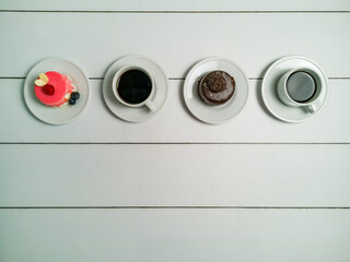 Colorful small fruity cupcakes on small white plates and cups of black coffee on light white background