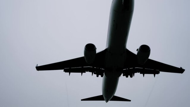Silhouette of large passenger airplane, airliner is flying in the overcast, grey sky - slow motion. Transportation, dark, mystery, gloomy, contrast look and flight concept