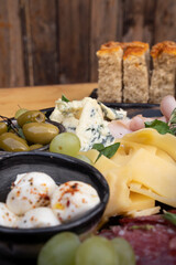Closeup view of a dish with italian spicy boconccinos, sliced pategras cheese, blue cheese, focaccia bread, green olives and ham with a wooden background.