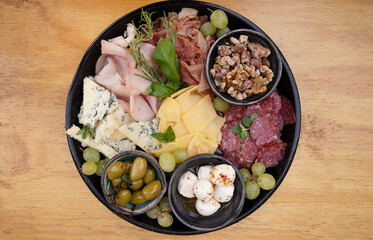 Cold cuts. Top view of a dish with sliced salami, cheese, blue cheese, italian boconccinos, walnuts, ham, cured ham and green olives, on the wooden table.