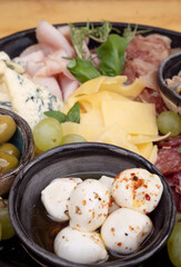 Food background. Closeup view of a dish boconccinos, salami, parmesan cheese, blue cheese, ham, cured ham and green olives.	