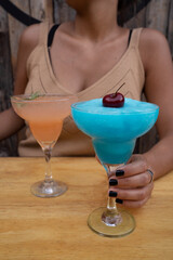 Night cocktails. closeup view of a young woman with two icy tequila based drinks. A blue citric Margarita frozen and a pink grapefruit Margarita.