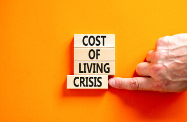 Cost of living crisis symbol. Concept words Cost of living crisis on wooden blocks. Beautiful orange table orange background. Businessman hand. Business cost of living crisis concept. Copy space.