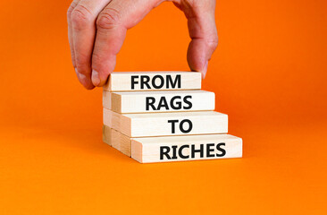 Rags or riches symbol. Concept words From rags to riches on wooden blocks. Beautiful orange table orange background. Businessman hand. Business rags or riches concept. Copy space.