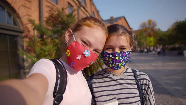 Teenagers with backpacks and protective masks take selfie on smartphone. Realtime