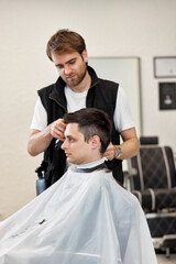 Fototapeta premium Barber shaving caucasian man in barber shop.