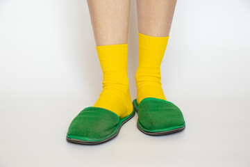 Female legs in yellow socks and green slippers on a white background