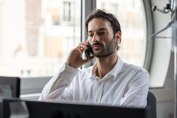 portrait d'un jeune homme souriant, employé de bureau assis devant son ordinateur au bureau. Il...