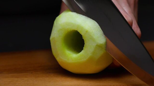 a sharp knife cuts a peeled apple. filmed in slow motion on a black background