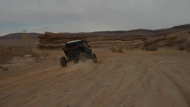 Tracking shot chasing behind UTV driving fast in red sandy wash in Utah desert