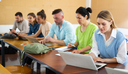 Fototapeta premium Group of students studying in the auditorium at study time, searches for information on a laptop and writes it out in a ..copybooks