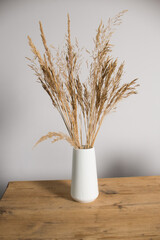 Dried flowers in a white vase stand on a wooden table
