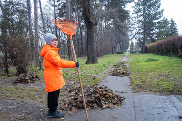Little child clean up lawn in front of house with rake. Sesonal problem - remove fallen leaves or...