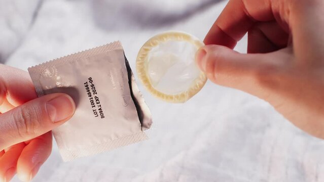 Woman opening condom, close up, Hand holding a condom in package, close up on bedroom background