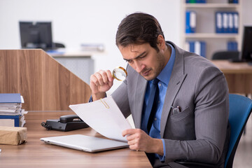 Young male auditor holding loupe at workplace