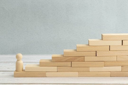 wooden figurine of a man stands on a staircase made of blocks on the first step.