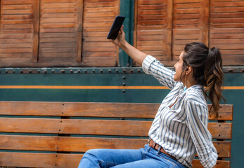 Outdoor picture of joyful positive female posing for a selfie sitting on bench.