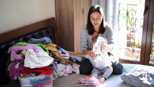 Mom And Little Girl Stack A Pile Of Laundry While Sitting On The Bed