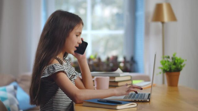 Preteen girl use laptop and talk on smartphone. Realtime