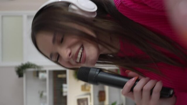 One woman young caucasian female teenager dancing alone at home with headphones on her head having fun while listen to the music happy smile real people self portrait UGC user generated content