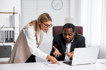 Angry female boss scolding African American office worker. A demanding manager-leader is annoyed by...