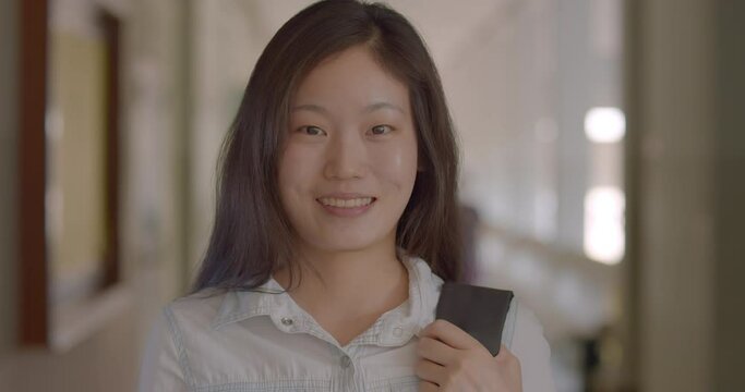 (Slow motion)A happy smiling Asian woman who is a Chinese teacher and teaches Chinese language in a secondary school of Thailand, standing with her laptop backpack.