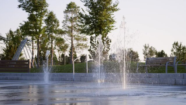Low view of splash pad water jets spraying at sunset when park is empty