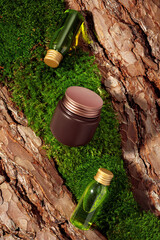 Two green glass cosmetic bottles and product mockup in brown and gold colors on textured tree bark and moss podium in sunlight. Mockup for the demonstration of cosmetic products