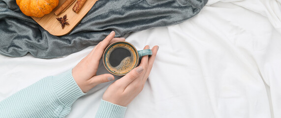 Woman holding cup of tasty pumpkin coffee on bed. Banner for design