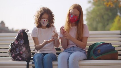 children in protective mask disinfect their hands outdoors. Realtime