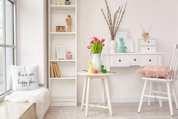 Vase with tulips, Easter eggs and rabbits on table in interior of living room