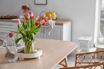 Vase with tulips, Easter eggs and jug of water on dining table in kitchen