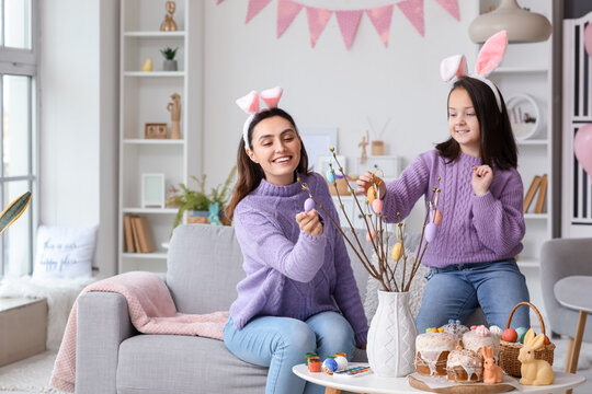 Little girl and her mother in bunny ears decorating tree branches with Easter eggs at home