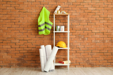 Fototapeta na wymiar Safety vest, shelving unit with renovation supplies and hardhat near brick wall