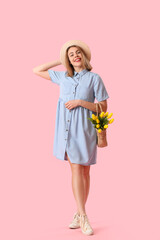 Young woman in hat with bag of tulips on pink background