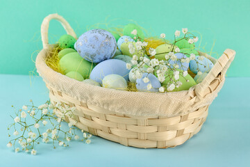 Basket with beautiful Easter eggs and gypsophila flowers on color background