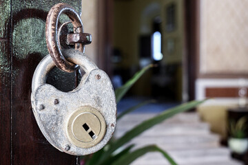 antique padlock hung on open wooden door. Out of focus background of a room illuminated with plants.