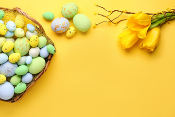 Fototapeta na wymiar Basket with painted Easter eggs and bouquet of tulip flowers on yellow background