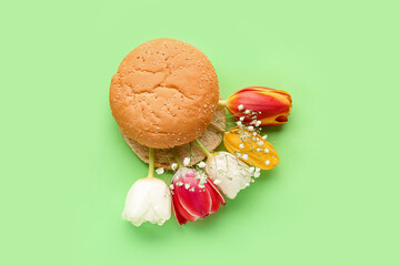 Creative composition with burger bun and beautiful flowers on green background