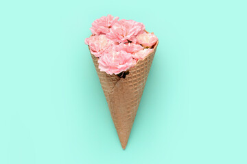 Waffle cone with beautiful carnation flowers on color background