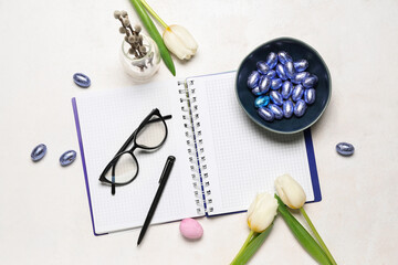 Notebook with eyeglasses, Easter eggs and tulips on white background