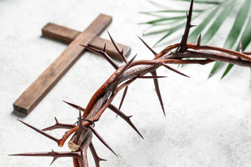 Crown of thorns with wooden cross and palm leaf on white grunge background, closeup. Good Friday concept