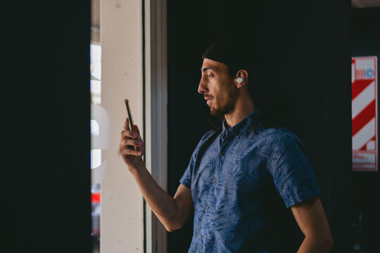 Young latin man watching a masterclass on his smart phone and listening to it through his wireless earphones.