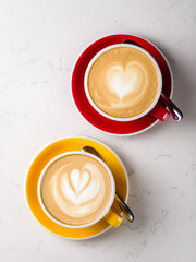 Two Cappuccino coffee with heart drawing at yellow and red cup on white marble table top view...