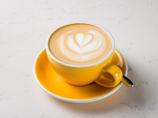 Cappuccino coffee with heart drawing on yellow cup on white marble table