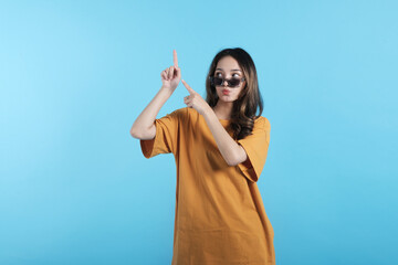 Asian young female using a sunglasses, gesture with her hands pointing to empty space on blue background