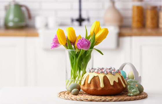 Easter cake, painted eggs, tulip flowers and bunny on table in kitchen