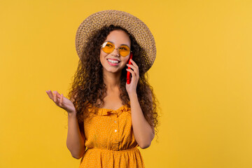 Attractive woman talking by phone, smiling. Young lady on yellow background.