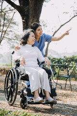 Asian young caregiver nurse support senior older male walking outdoors. Specialist girl doctor help and take care of elderly mature man patient doing physical therapy in public park at nursing home.