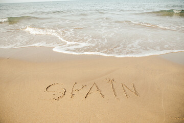 Spain lettering on the beach with wave and clear blue sea. 